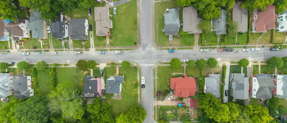 Houses on green lots along two streets that cross, with trees and parked cars, seen from directly above