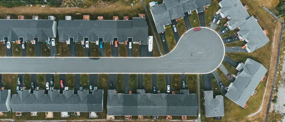 Rows of townhouses with grey roofs and short driveways along a street that ends in a round turning circle, seen from directly above
