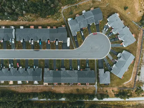 Rows of townhouses with grey roofs and short driveways along a street that ends in a round turning circle, seen from directly above